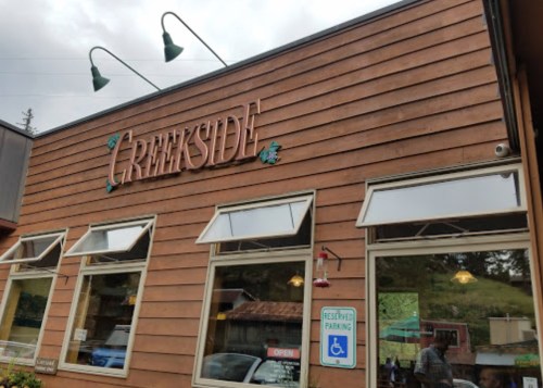 Exterior of a wooden building with the sign "Creekside," featuring large windows and a reserved parking sign.