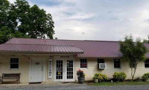 A welcoming building with a metal roof, "OPEN" sign, and flower pots outside, set against a cloudy sky.