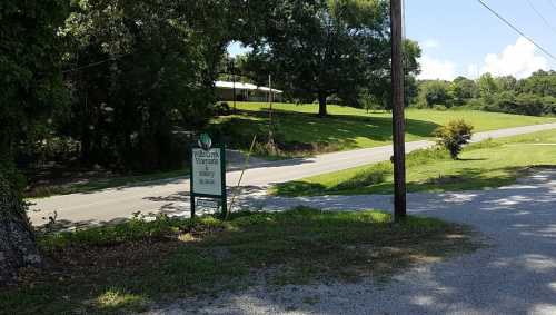 A roadside view featuring a sign for a venue, with green grass and trees in the background under a clear blue sky.