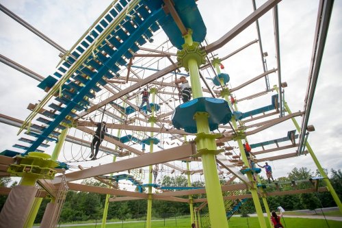 A colorful outdoor ropes course with various climbing structures and people navigating the obstacles.
