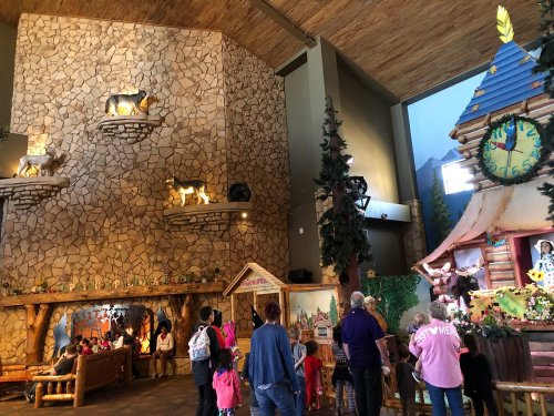 A cozy indoor space with a stone wall, wooden decor, and families enjoying a whimsical performance.