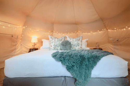 Cozy interior of a glamping tent featuring a plush bed, decorative pillows, and soft lighting.