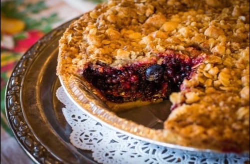 A freshly baked berry pie with a crumbly topping, partially sliced, on a decorative plate.