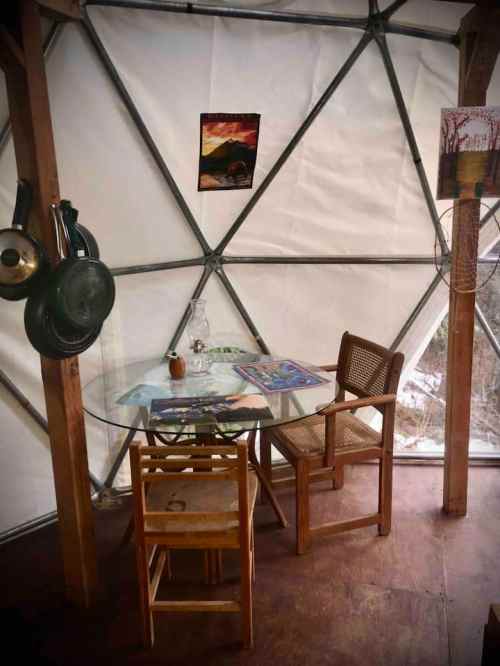 A cozy interior of a geodesic dome with a glass table, wooden chairs, and a wall poster.