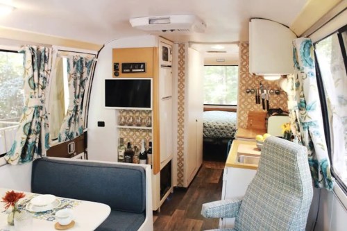 Cozy interior of a vintage camper, featuring a dining area, kitchenette, and a bedroom in the background.