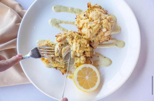 A plate of crab cakes drizzled with sauce, garnished with a lemon slice, and a fork cutting into one cake.