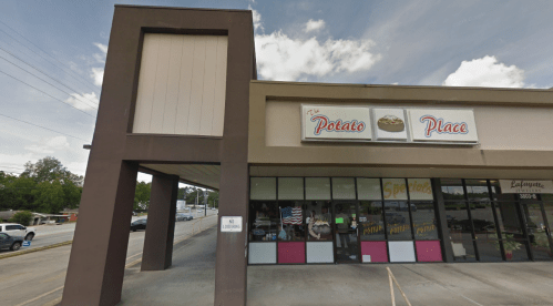 Exterior view of "The Potato Place," a storefront with large windows and a sign, set against a cloudy sky.