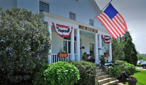 A historic building with an American flag and decorative bunting, surrounded by greenery.