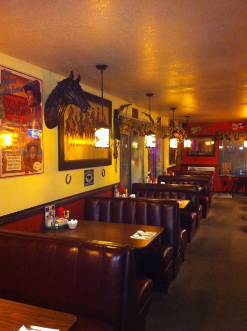 Cozy restaurant interior with leather booths, western decor, and vintage posters on the walls. Warm lighting creates a welcoming vibe.