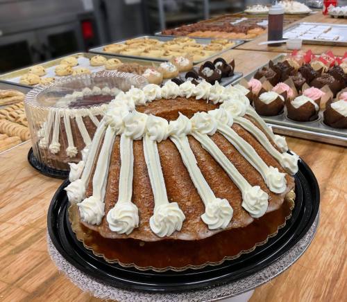 A decorated bundt cake with cream frosting, surrounded by various baked goods on a table.