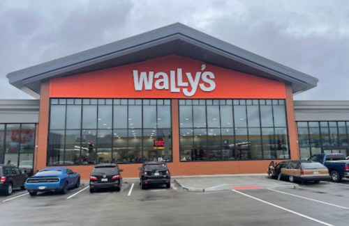 Exterior of Wally's store with large windows and an orange sign, surrounded by parked cars on a cloudy day.