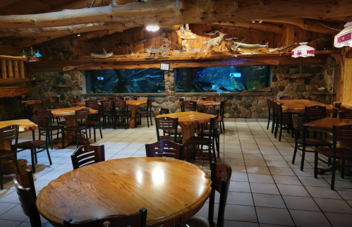 Cozy restaurant interior with wooden decor, tables, and a large aquarium in the background.