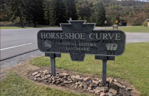 Sign for Horseshoe Curve, a National Historic Landmark, located near a road with trees in the background.