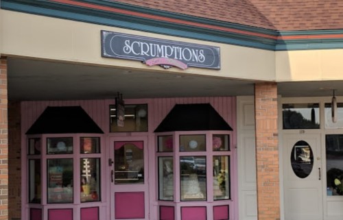 A storefront with a pink and black sign reading "Scrumptions," featuring large windows and a welcoming entrance.