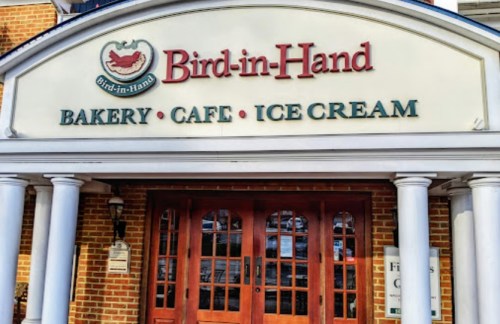 Sign for "Bird-in-Hand" featuring Bakery, Cafe, and Ice Cream, with a brick building and wooden doors.