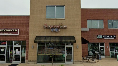 Exterior of a shopping plaza featuring a storefront for "Sugarfire Pie" with a black awning and nearby businesses.