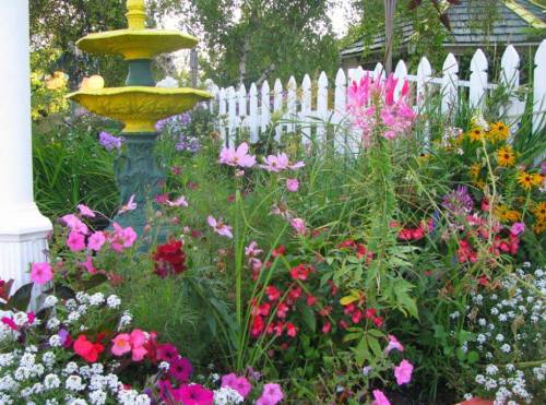 A vibrant garden filled with colorful flowers and a decorative fountain surrounded by a white picket fence.