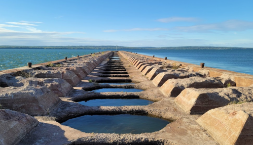 A long pier extends into the water, featuring rectangular pools along its surface, under a clear blue sky.