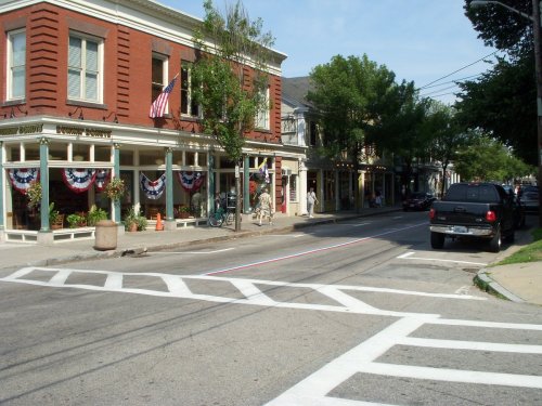 A quaint street scene featuring brick buildings, patriotic decorations, and parked cars under a clear blue sky.