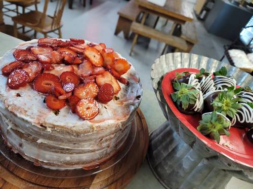 A layered cake topped with fresh strawberries next to a platter of chocolate-covered strawberries.