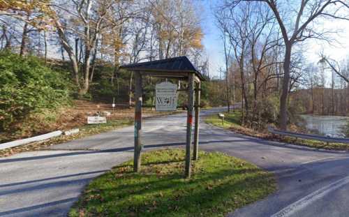 Sign at a fork in the road, surrounded by trees and greenery, indicating directions to a well and nearby areas.