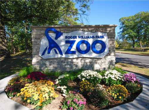 Sign for Roger Williams Park Zoo, featuring a blue logo and colorful flowers in front.