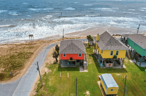 Aerial view of colorful beach houses near the shore, with waves crashing on the sandy beach and a clear sky.