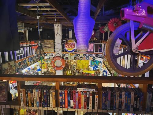 A colorful, eclectic indoor space filled with vintage items, decorations, and a collection of VHS tapes on a shelf.