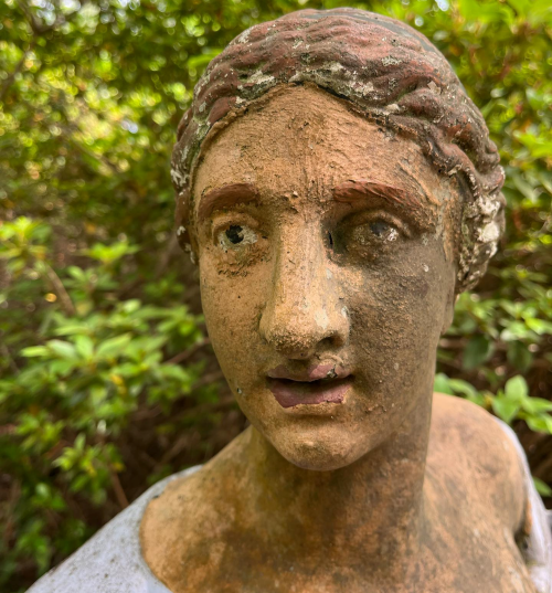 A weathered statue of a woman with a serene expression, partially obscured by greenery.