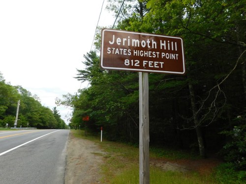 Sign for Jerimoth Hill, the highest point in the state, at 812 feet, alongside a tree-lined road.