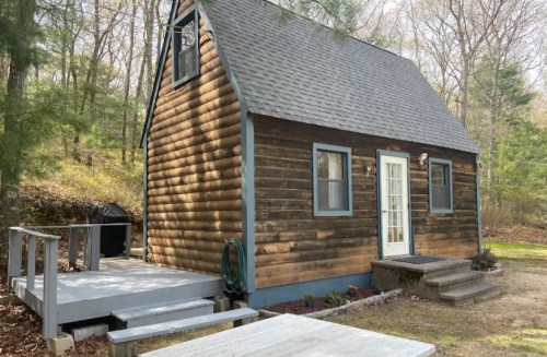 A small wooden cabin with a sloped roof, front porch, and surrounded by trees in a natural setting.