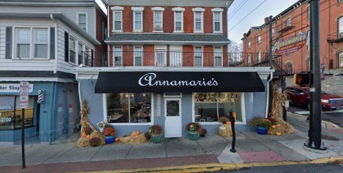 A storefront with a black awning reading "Annamarie's," decorated with pumpkins and hay bales for fall.