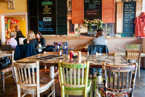 A cozy café interior with colorful chairs, a large table, and patrons enjoying their meals in a vibrant atmosphere.
