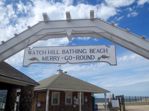Sign for Watch Hill Bathing Beach and Merry-Go-Round, with a blue sky and clouds in the background.