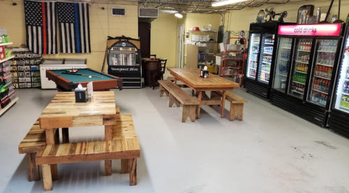 Interior of a casual space with wooden tables, a pool table, and a drink fridge, featuring an American flag on the wall.