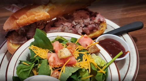 A plate with a sandwich filled with roast beef and a side salad topped with tomatoes, cheese, and croutons.