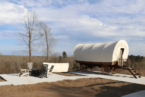A covered wagon on a concrete pad, with outdoor seating nearby and a scenic view of trees and sky in the background.