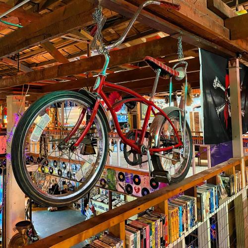 A red bicycle hangs from the ceiling in a vibrant, eclectic space filled with records and colorful decor.
