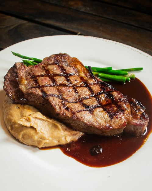A grilled steak with a crosshatch pattern, served with mashed potatoes and green beans on a white plate.