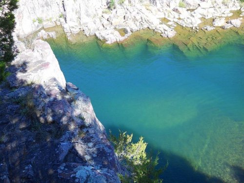 A rocky cliff overlooking a clear, turquoise body of water surrounded by natural vegetation.