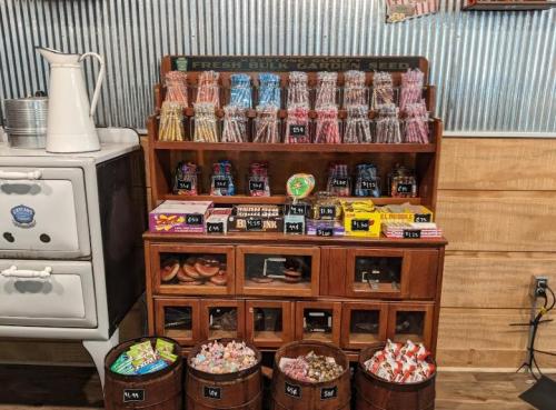A vintage display with jars of candy and seeds, wooden bins of sweets, and a retro stove in a rustic setting.