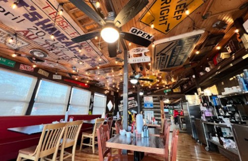 Cozy restaurant interior with wooden tables, ceiling fans, and eclectic signs hanging from the ceiling.