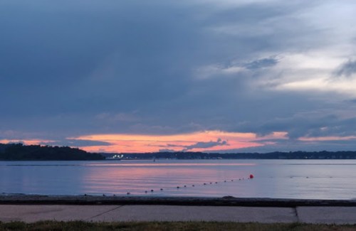 A serene lake at sunset, with colorful clouds reflecting on the water and a calm shoreline in the foreground.