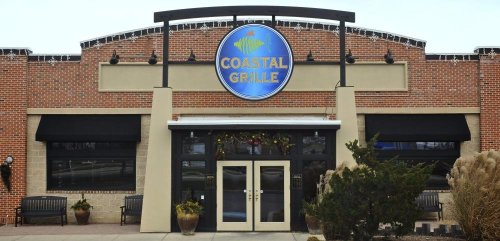 Exterior of Coastal Grille restaurant featuring a blue sign, brick facade, and festive decorations.