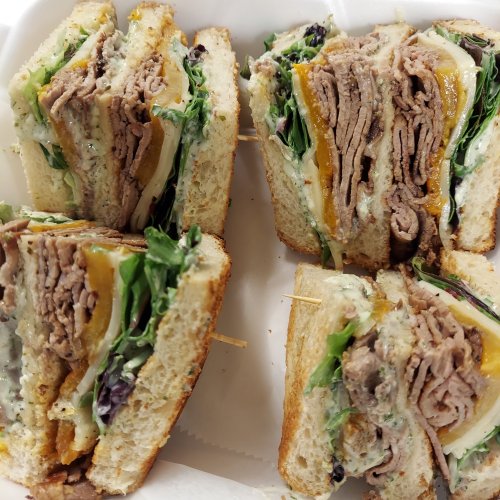 A close-up of a stacked sandwich with layers of roast beef, cheese, and greens, held together with toothpicks.