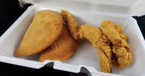 A takeout container with two golden empanadas and several crispy chicken tenders.
