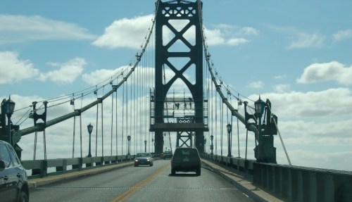 A view of a suspension bridge with cars driving on it under a blue sky with clouds.