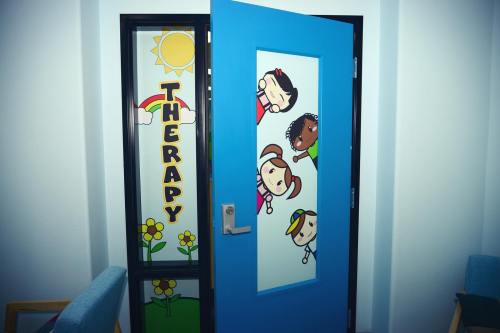 A colorful door labeled "THERAPY" with cheerful cartoon characters and a sunny design.