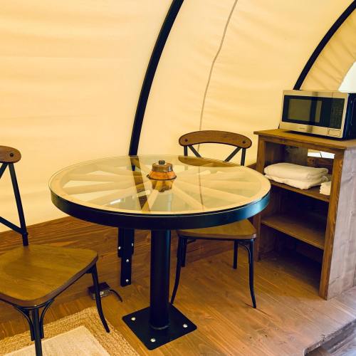Cozy interior of a glamping tent featuring a round table, two chairs, a microwave, and a wooden shelf.