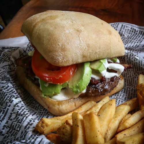 A delicious sandwich with beef, lettuce, tomato, avocado, and mayo, served with a side of golden fries.